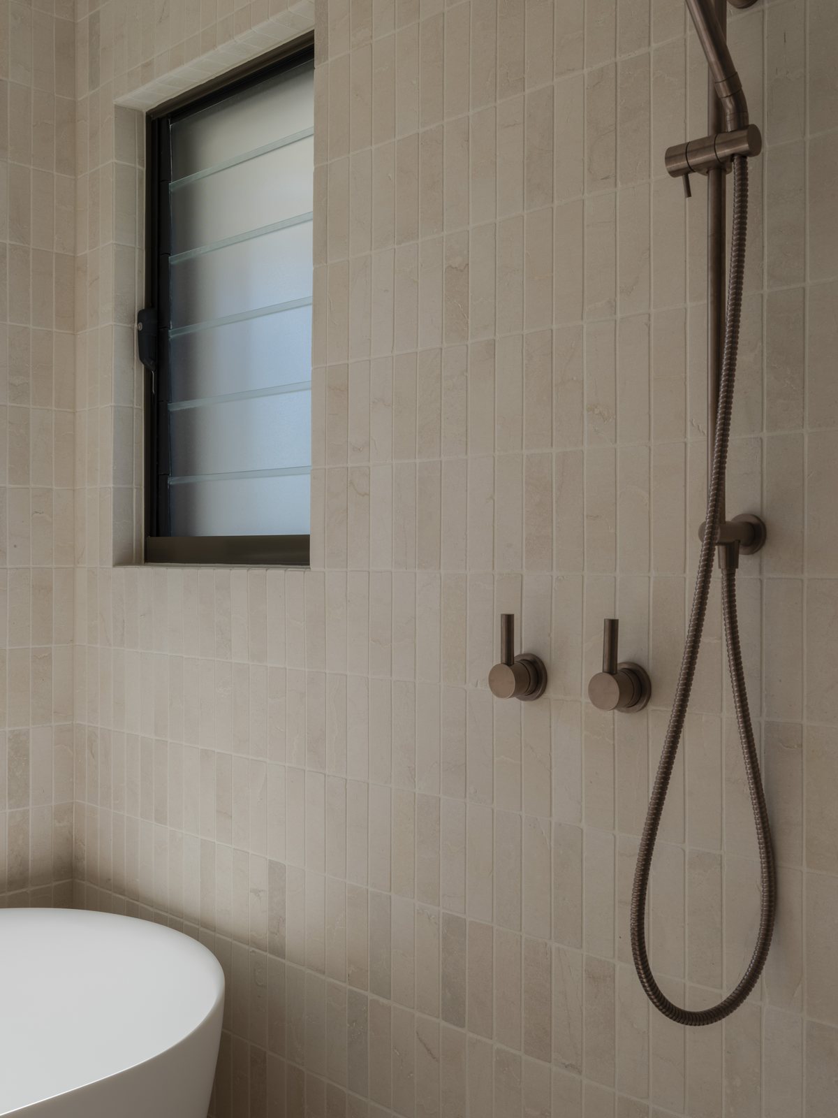 Freestanding bath and brushed bronze shower mixers below a louvre window in a Gold Coast bathroom renovation