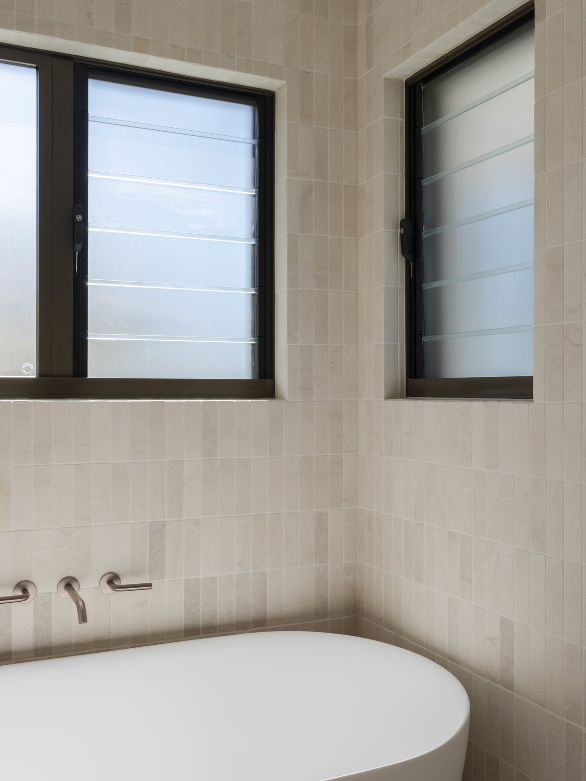 Freestanding bath beneath louvre windows with brushed bronze wall mixers in a Gold Coast bathroom renovation