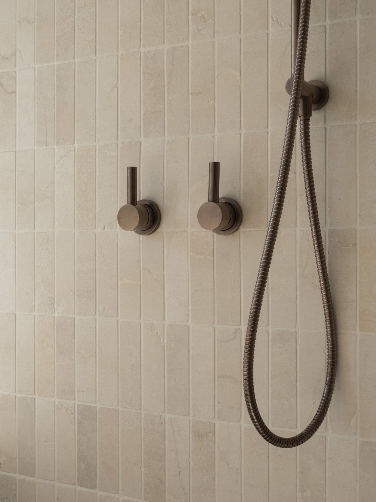 Brushed bronze shower mixers and handheld rail on stack-bond stone tiling in a Gold Coast bathroom renovation