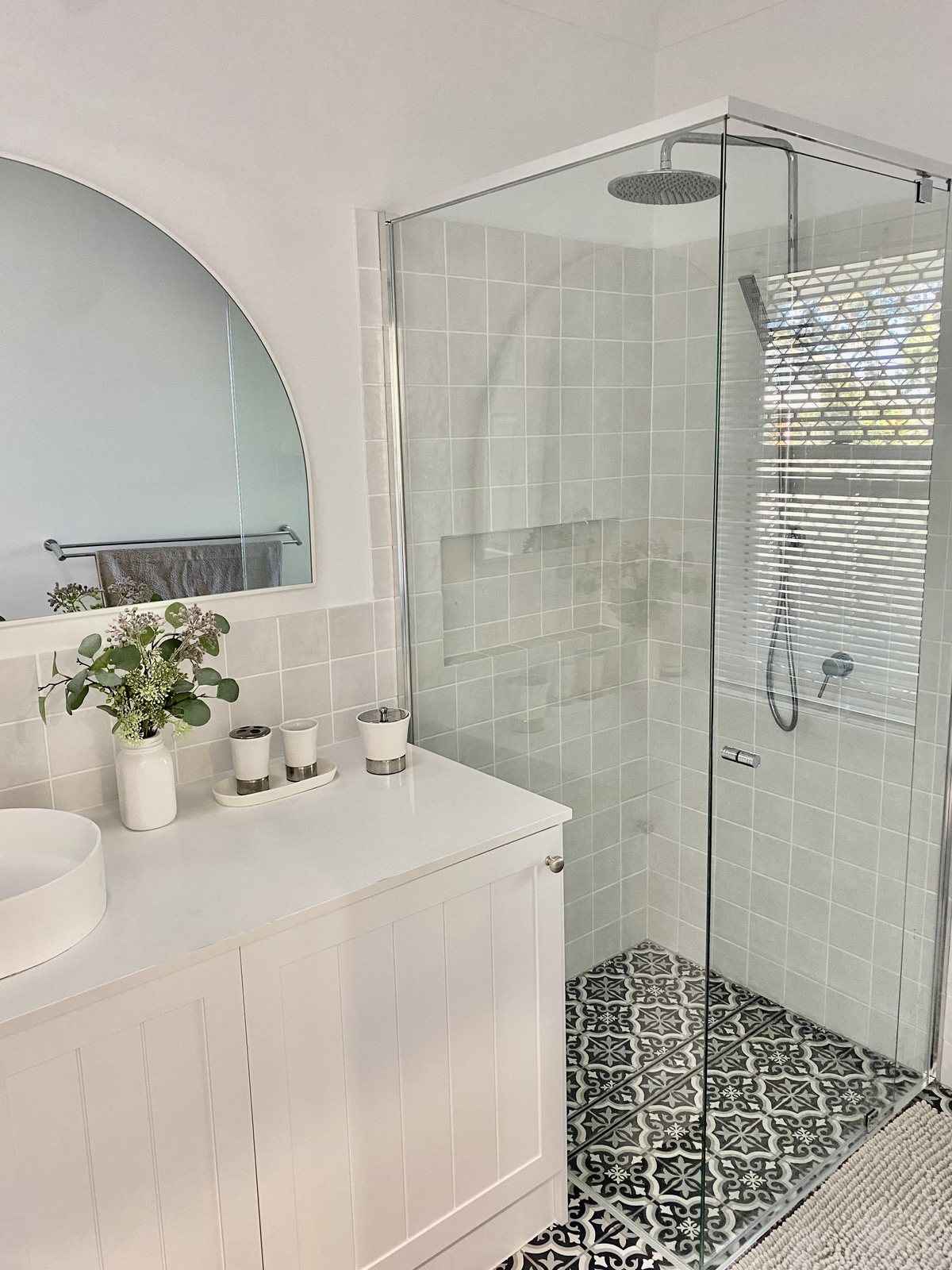 White cottage-style bathroom renovation with a tiled walk-in shower and patterned floor tiles