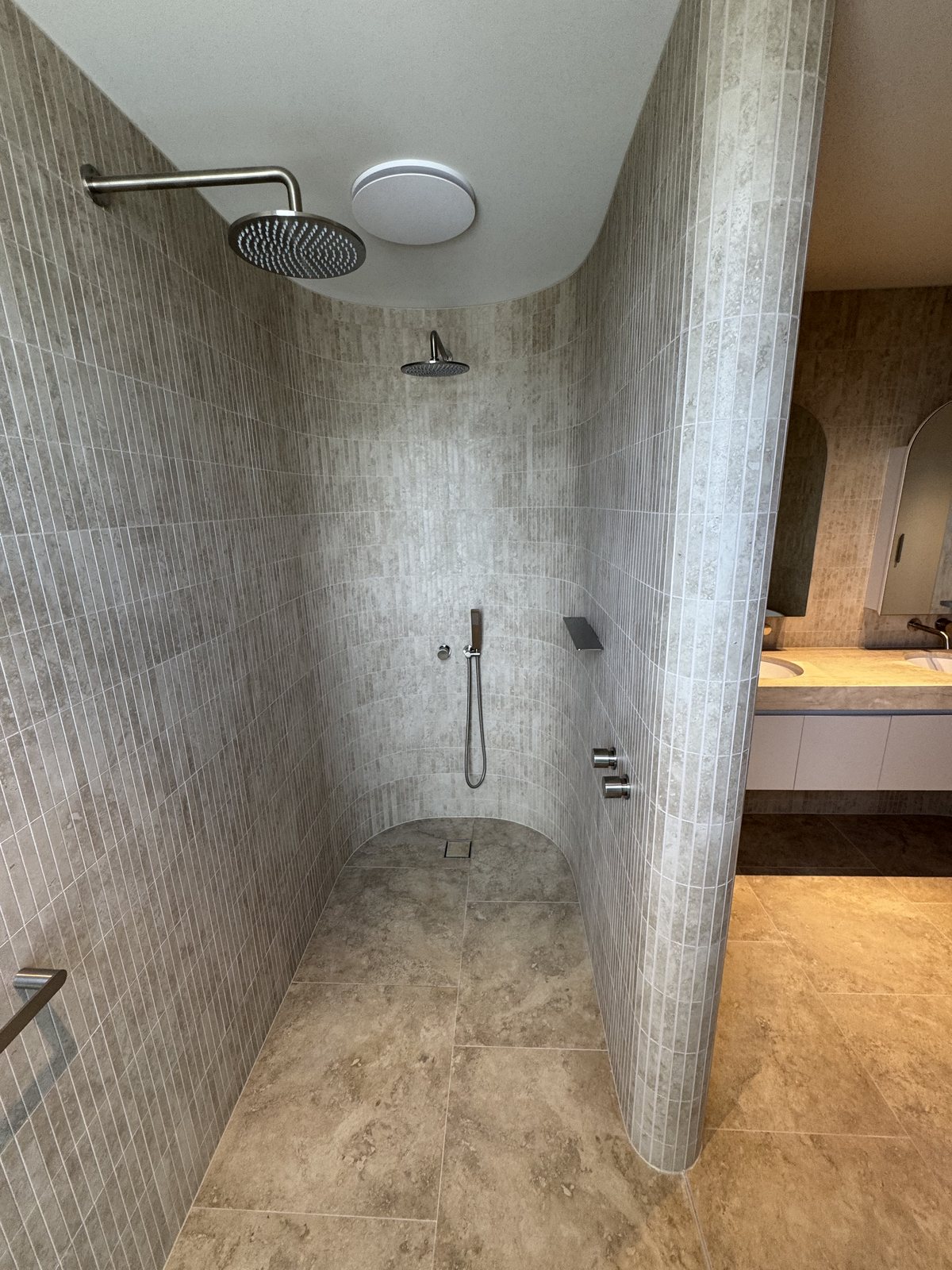 Curved walk-in shower with rain heads and travertine tiling in a Gold Coast bathroom renovation