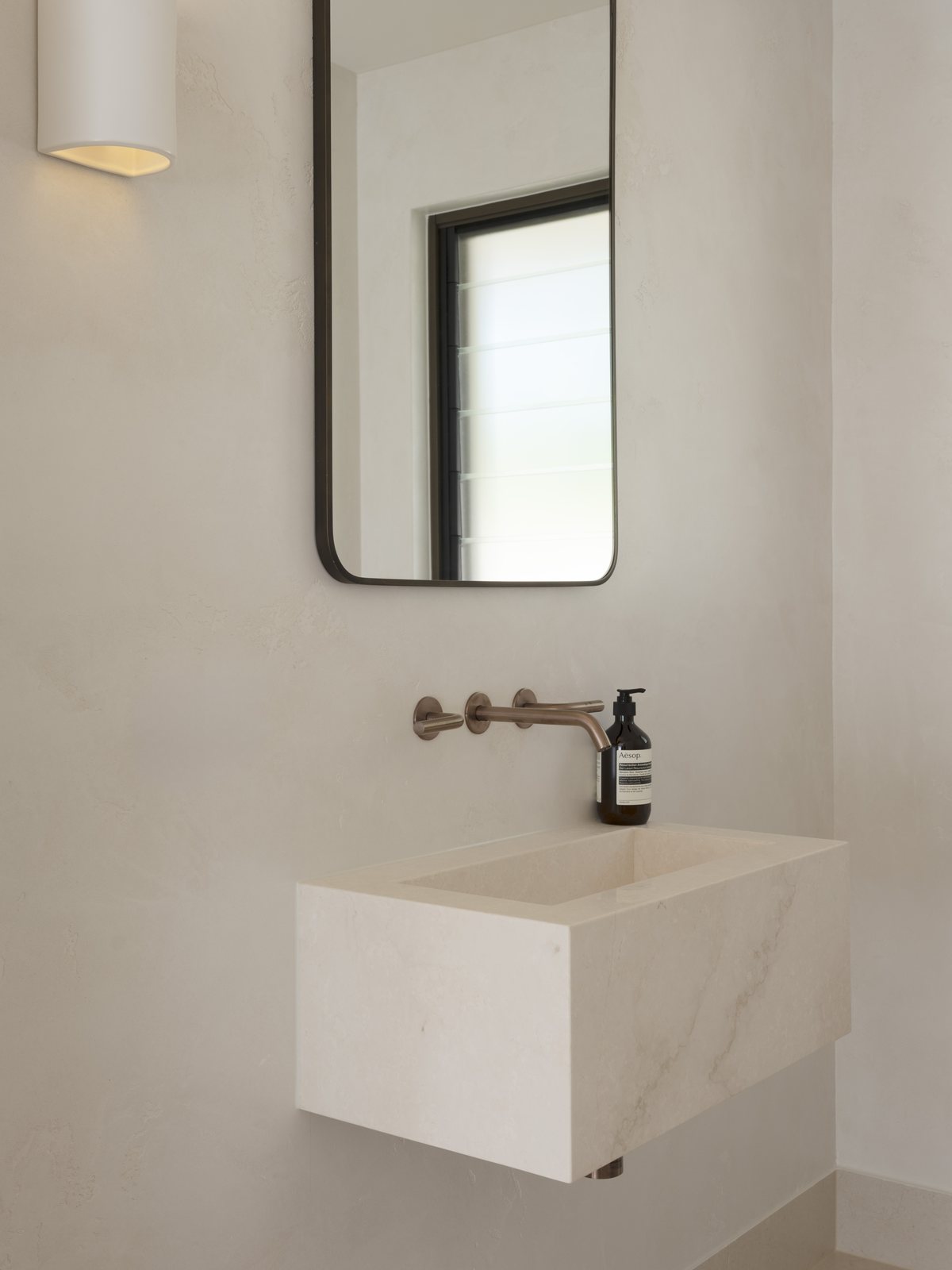 Wall-hung stone basin with a brushed bronze wall mixer and tall mirror in a Gold Coast powder room renovation