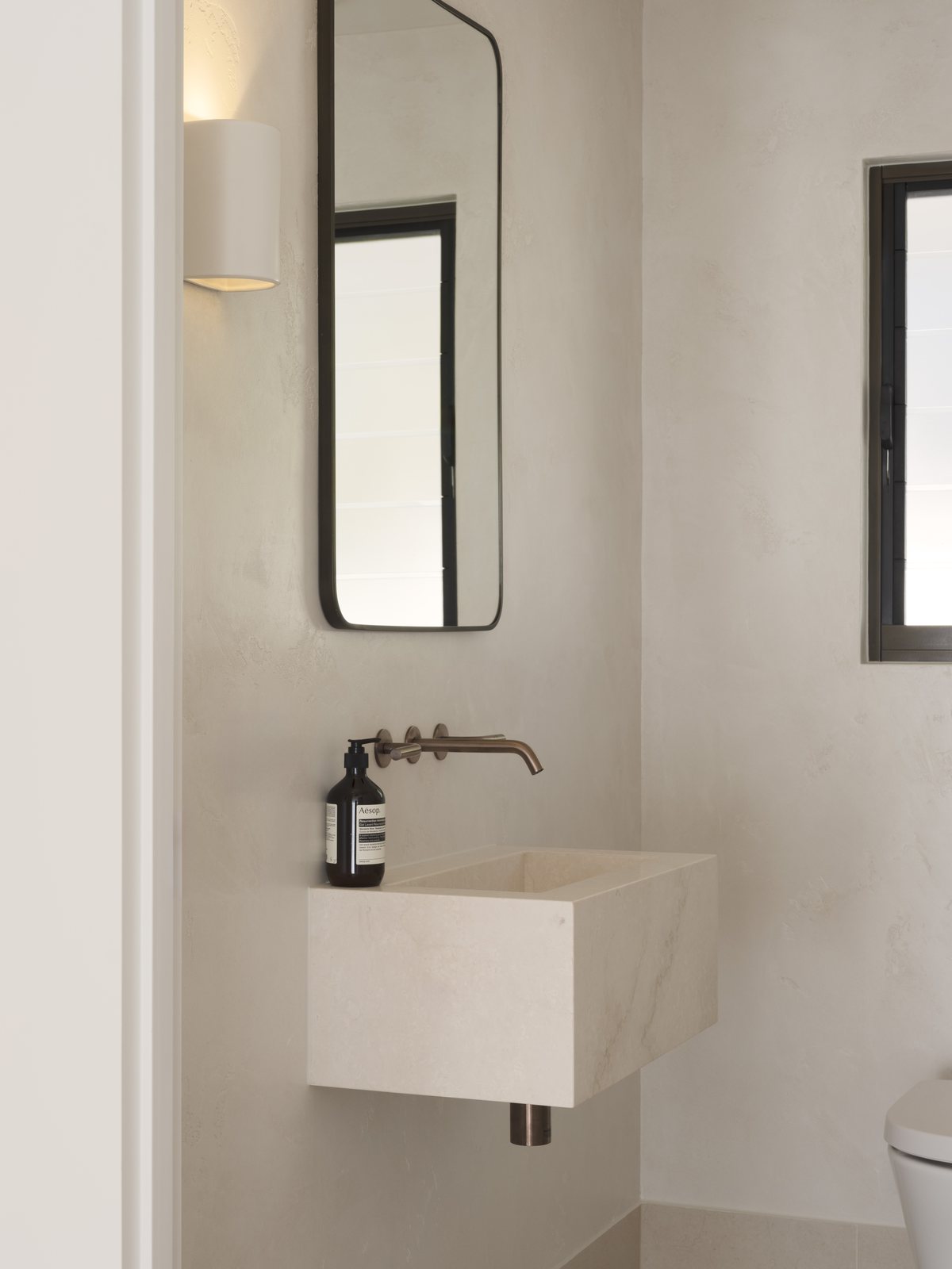 Gold Coast powder room renovation with a wall-hung stone basin, tall mirror and bronze wall mixer