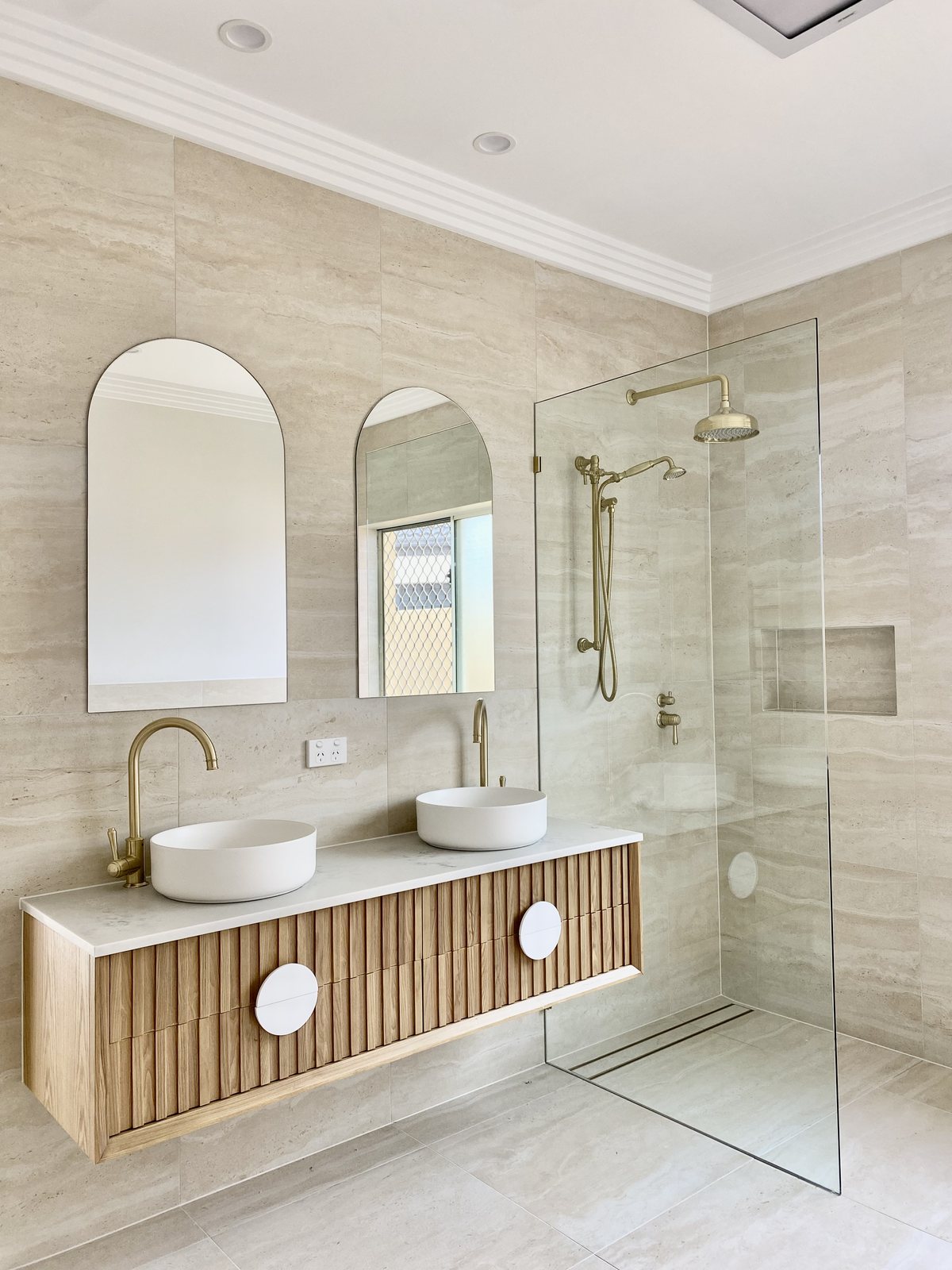 Renovated Gold Coast ensuite with travertine-look tiling, a fluted timber double vanity and brass tapware