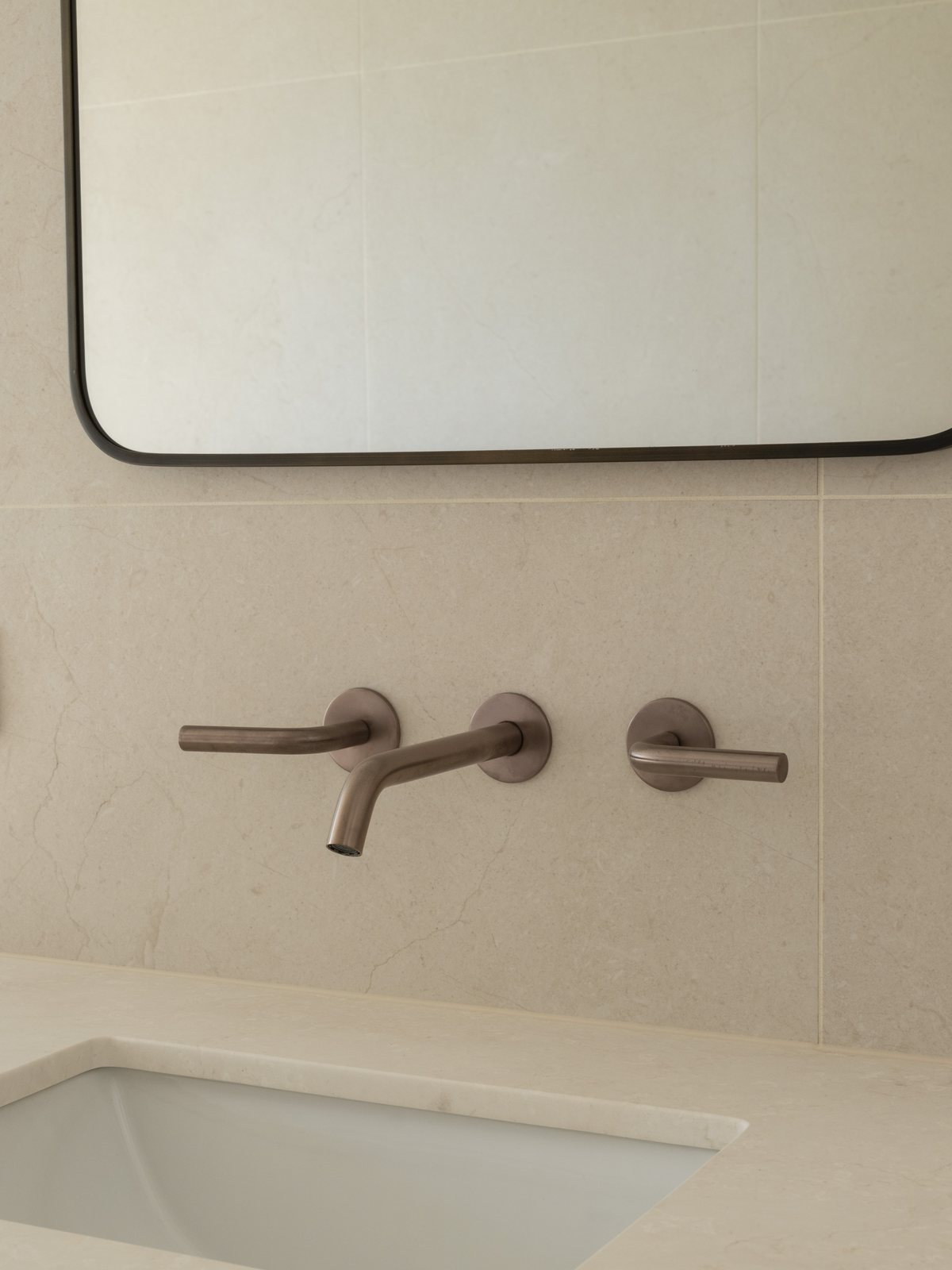 Floating stone vanity with an undermount basin, round mirror and brushed bronze mixer in a Gold Coast bathroom renovation